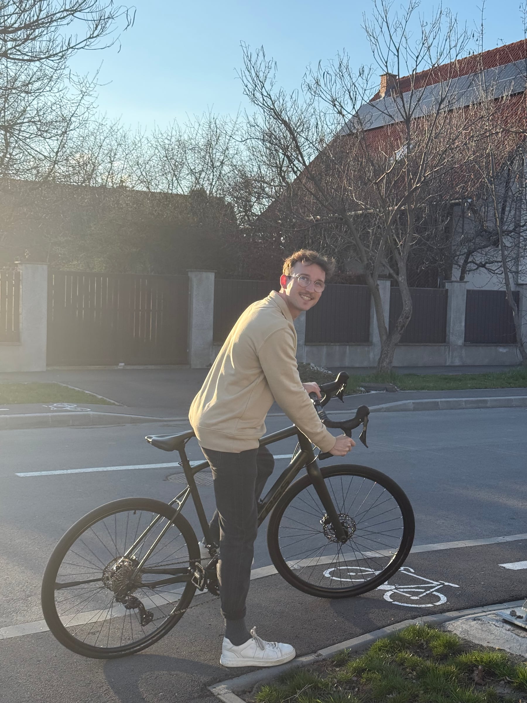 Krisztián standing beside his bicycle in warm evening light