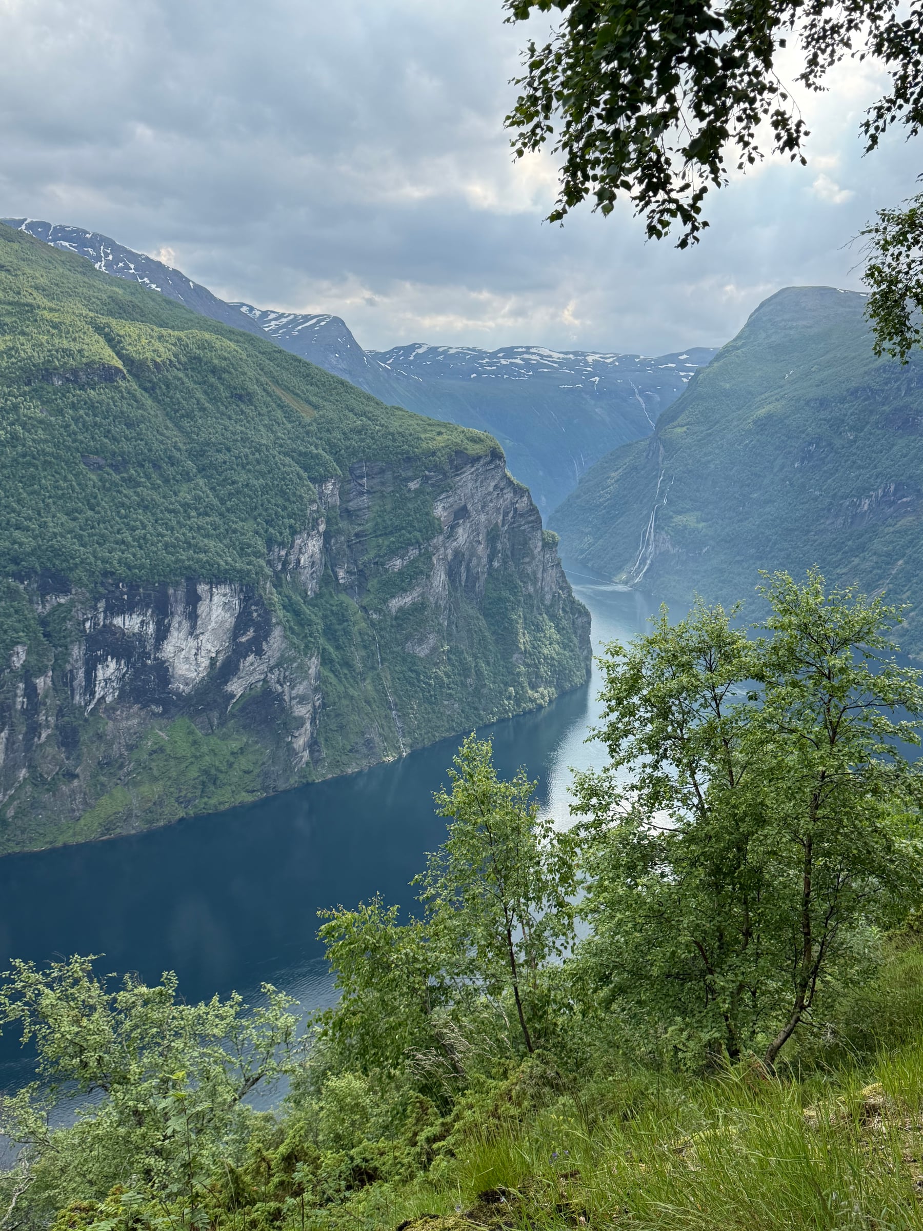 A still fjord reflecting mountains beneath a clouded sky.